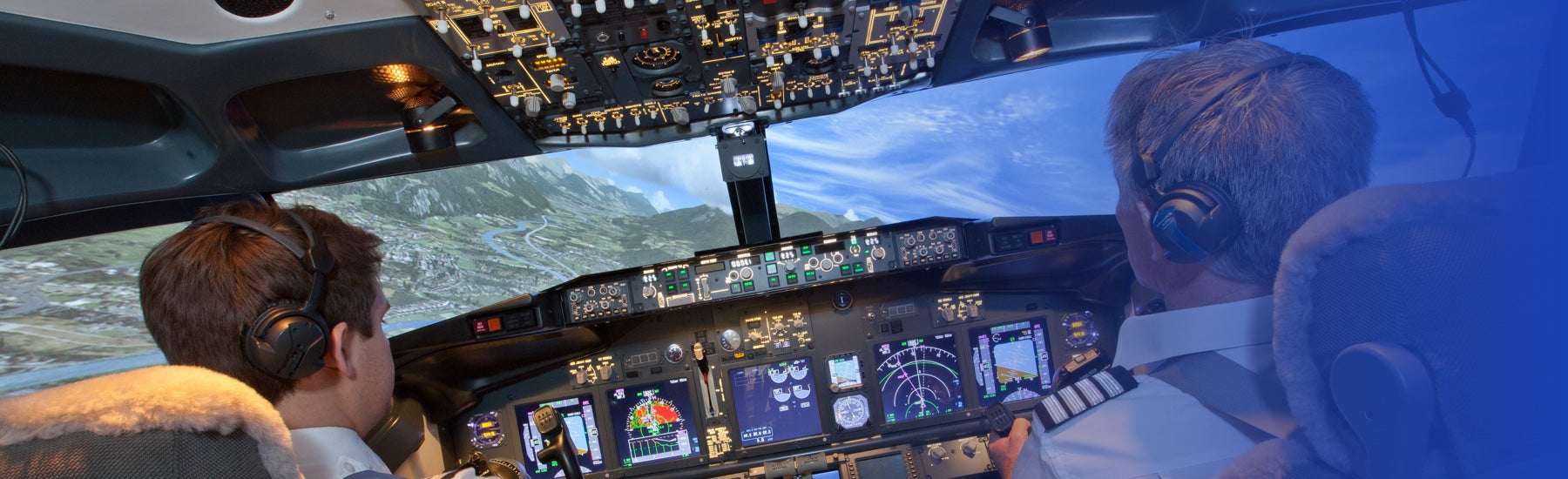 Two people in a flight simulator manoeuvre through hilly terrain while attempting to land.