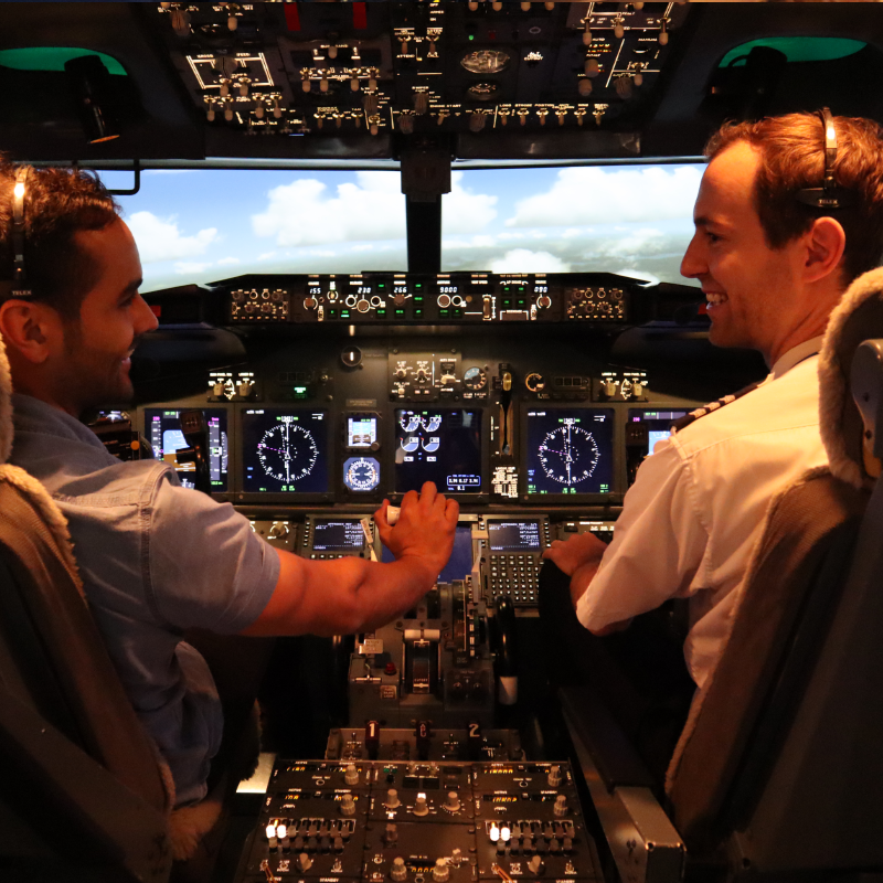 Two people look and smile at each other inside of a flight simulator cockpit at Flight Experience Perth