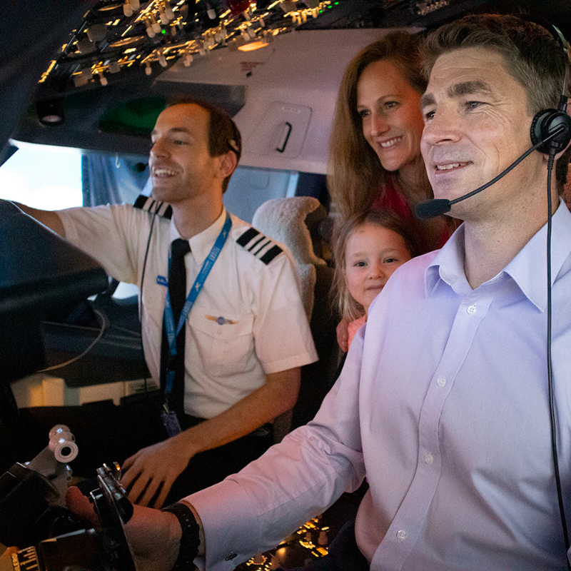 A family sits inside of the cockpit of a Boeing 737 flight simulator, a flight instructor guides them