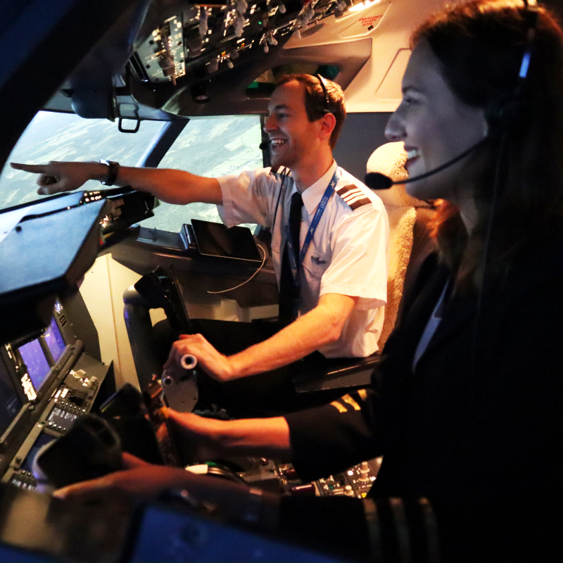 A male flight instructor inside of a flight simulator points something out to a female customer