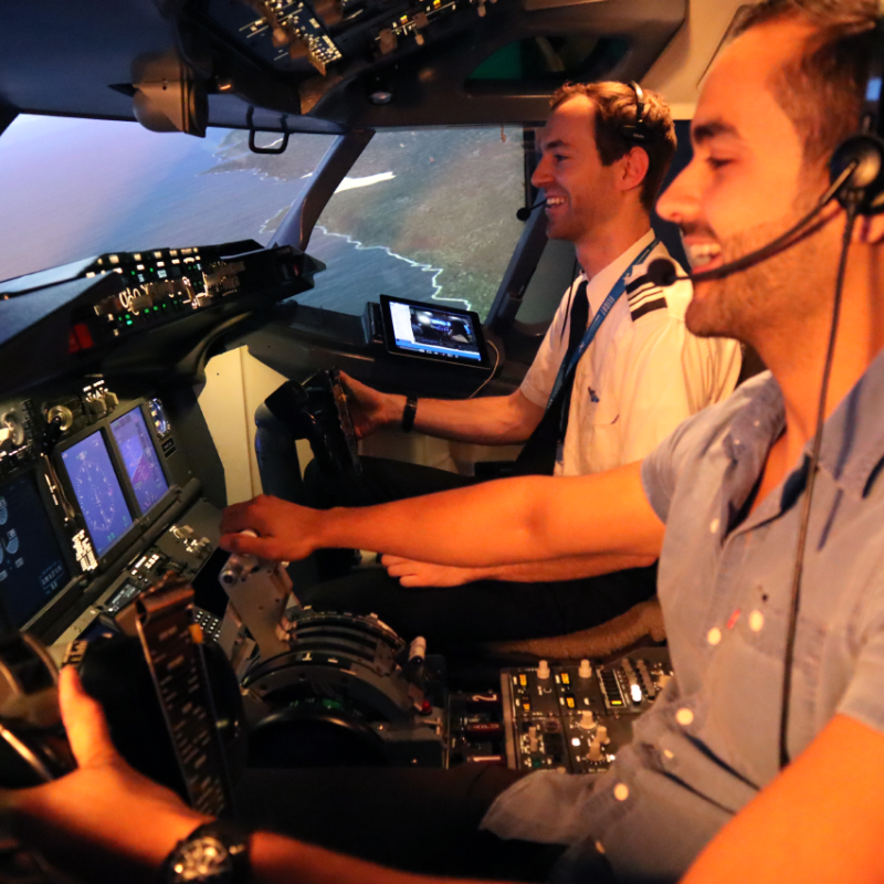 Two pilots laugh and smile together while sitting inside an aeroplane simulator cockpit.